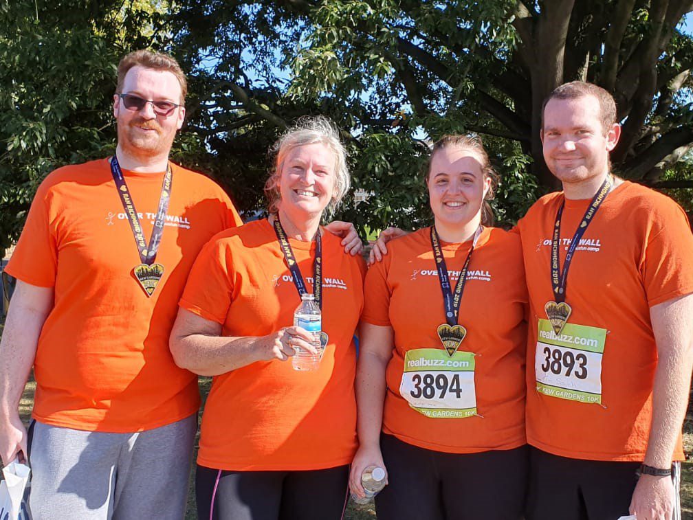 Four men and women in orange Over The Wall t-shirts who have just fundraised and gained a medal.