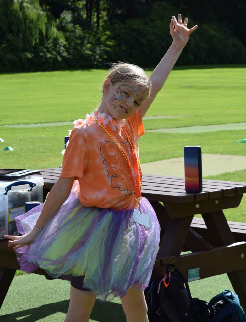 Child in orange camp t-shirt and tutu in a dancing pose and big smile on there face