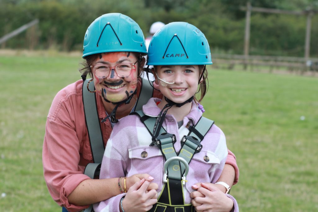 Mother and daughter at Over The Wall Family Camp wearing helmets ready to abseil. Young girl has a feeding tube.