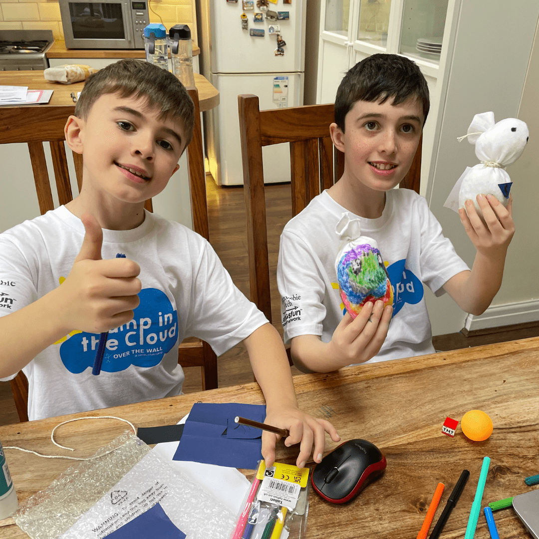 Two brothers in their Camp in the Cloud t-shirts are smiling at the camera with their crafts. One of the brothers is holding his thumb up