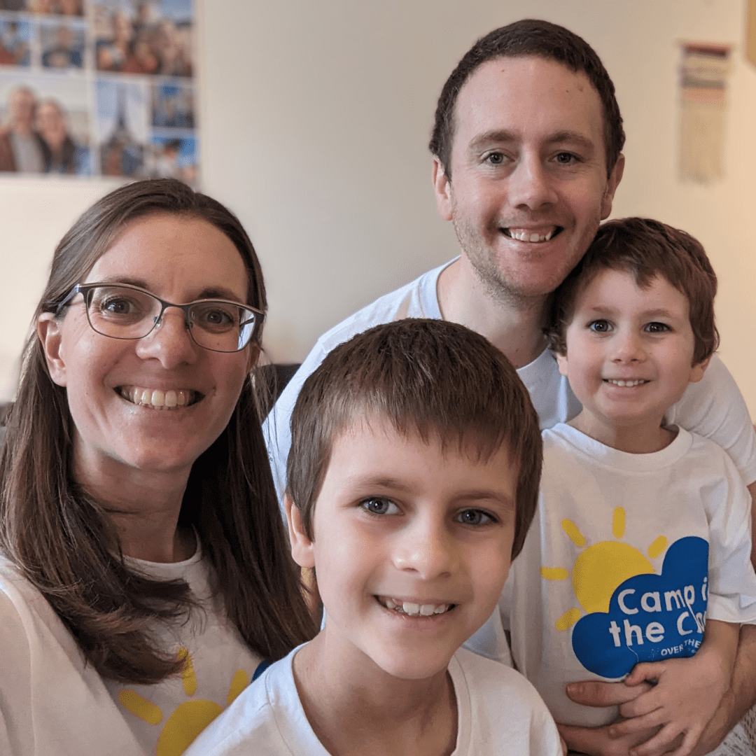 A selfie taken by a family of 4, Mum, Dad and two children. They are all wearing their Camp in the Cloud t-shorts and smiling at the camera