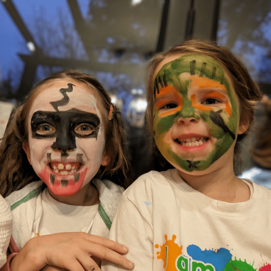 Two small girls smiling at the camera. They have Halloween themed face paint on