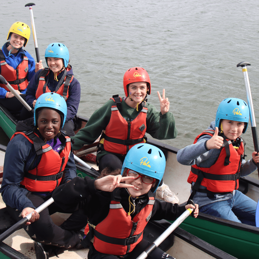 Children and young people sat in kayaks smiling at the camera