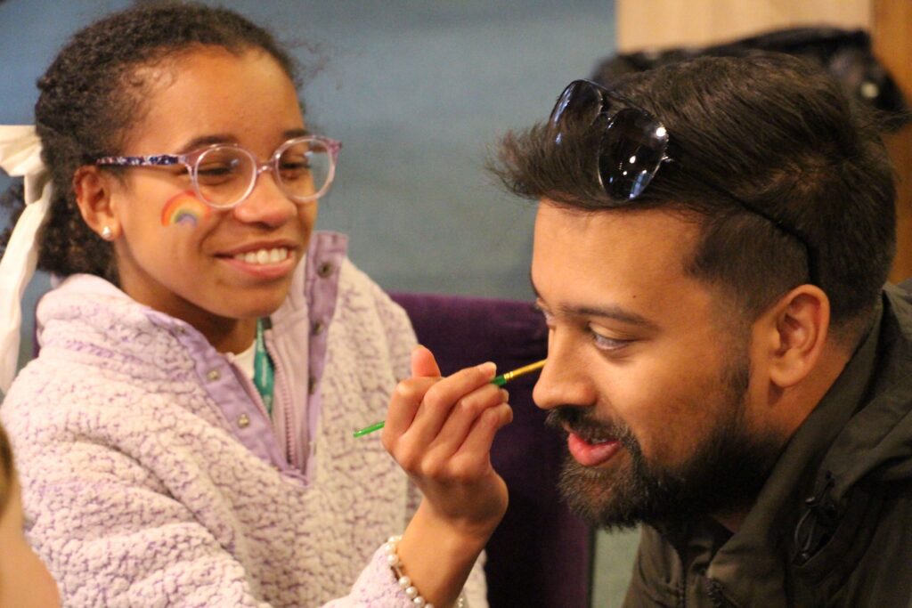 Young girl smiling while painting the face of an adult