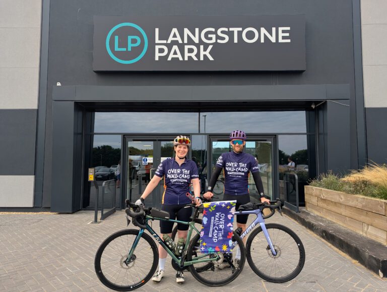 Man and woman in Over The Wall Camp cycling tops with bikes standing outside offices in Havant