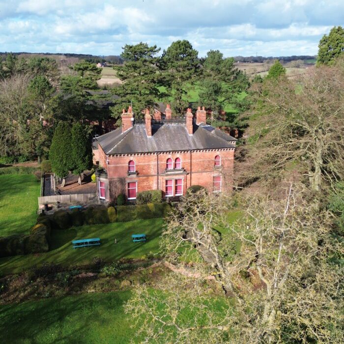 Red brick school building nestled amongst trees and grounds