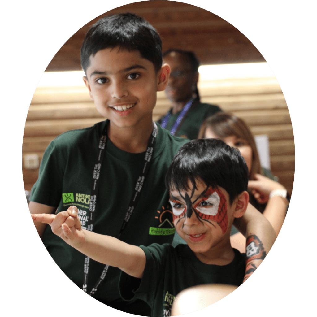 Two young boys in green t-shirts smiling, one with spiderman facepaint