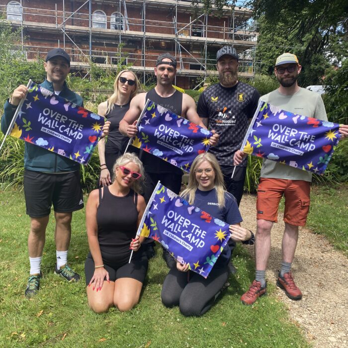 Group of people in walking gear holding Over The Wall Camp flags smiling
