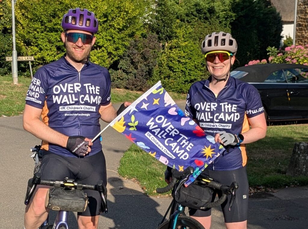 two cyclists in Over The Wall Camp shirts with flags