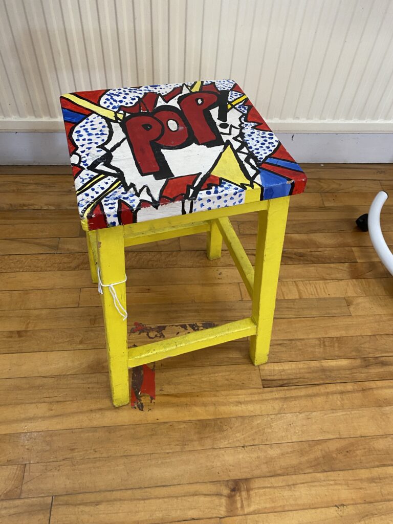 A painted wooden stool with the word 'pop' on it
