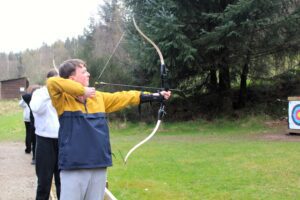 Ben taking aim at an archery target with a bow and arrow