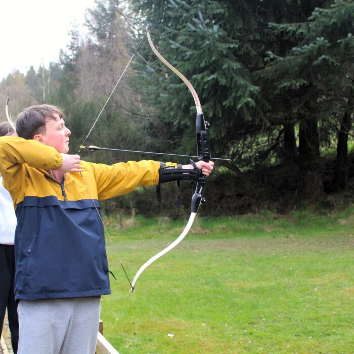 Ben taking aim at an archery target with a bow and arrow